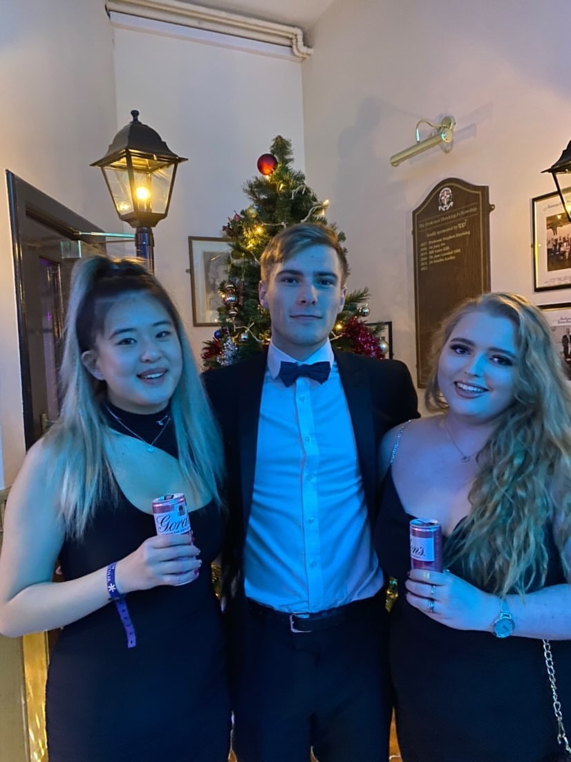 Three students holding drinks, in black tie outfits