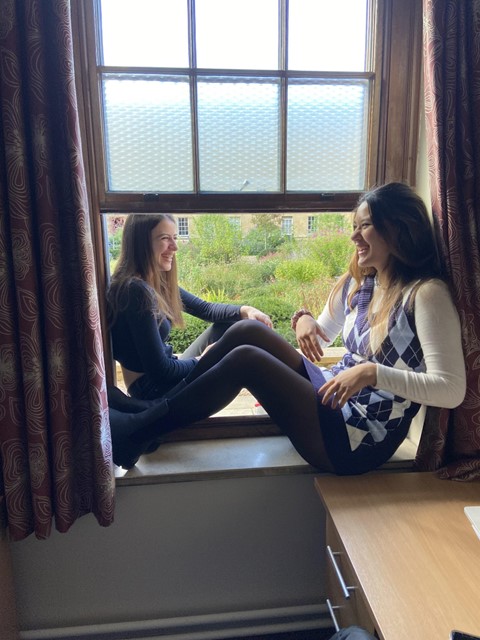 Two students sat on a windowsill, either side of the window, laughing