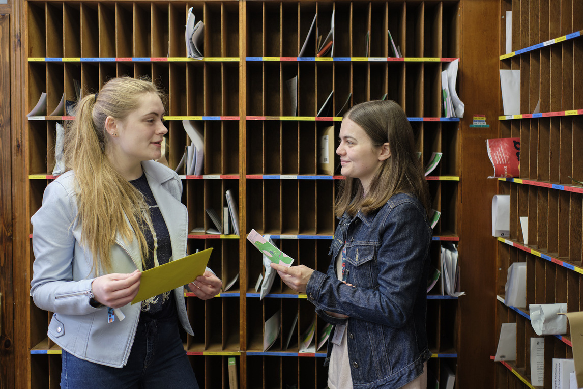 Two students chatting in front of pigeon holes in the porters' lodge