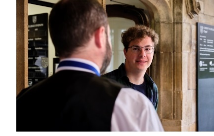 A young man talking to a porter outside the porters lodge of Christ's College, Cambridge.