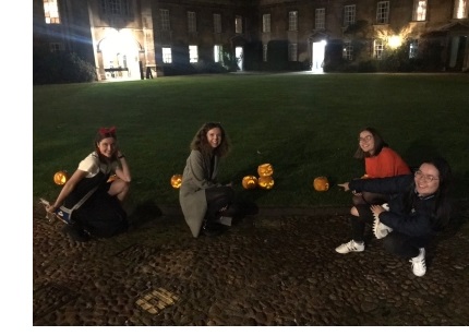 Iona and three friends with carved pumpkins in First Court at Christ's College, Cambridge, at night.