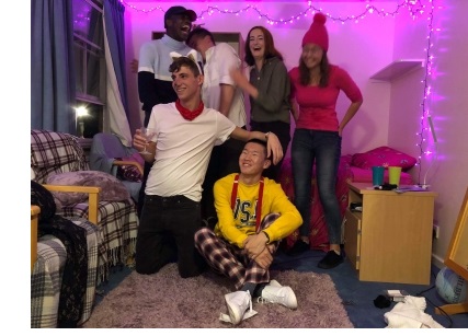 Hannah and a group of students in fancy dress, in a purple-walled room lit by fairy lights.