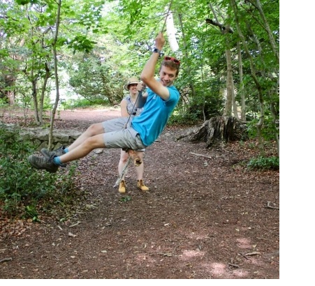 A man in a blue t-shirt being pushed on a rope swing by a female friend.