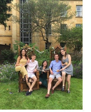 A group of students, two sat on wooden thrones, in smart summer clothing in a sunny garden.