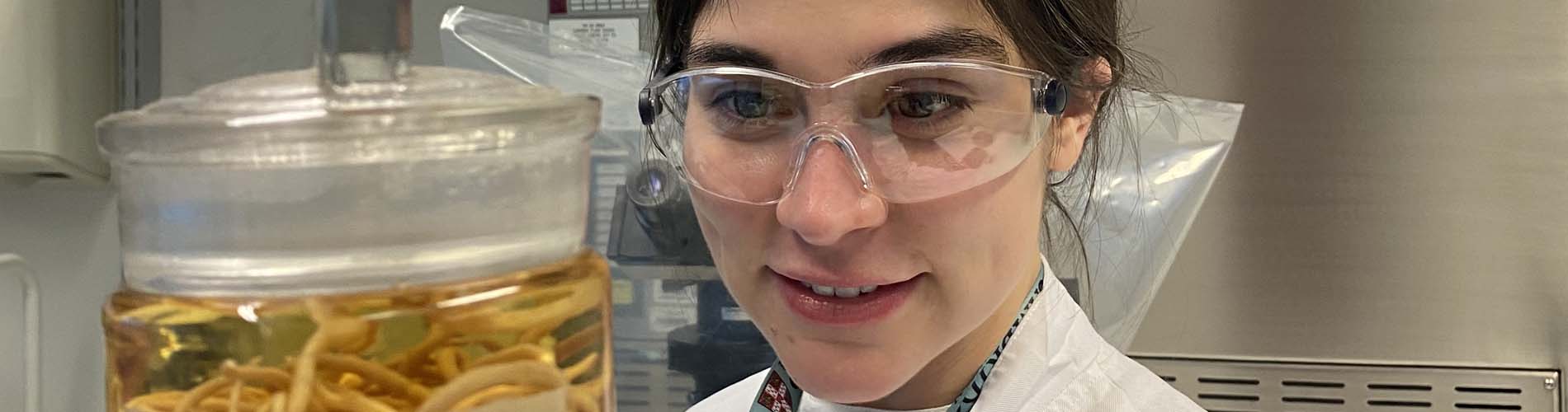 Scientist wearing protective glasses looking at a jar of worms