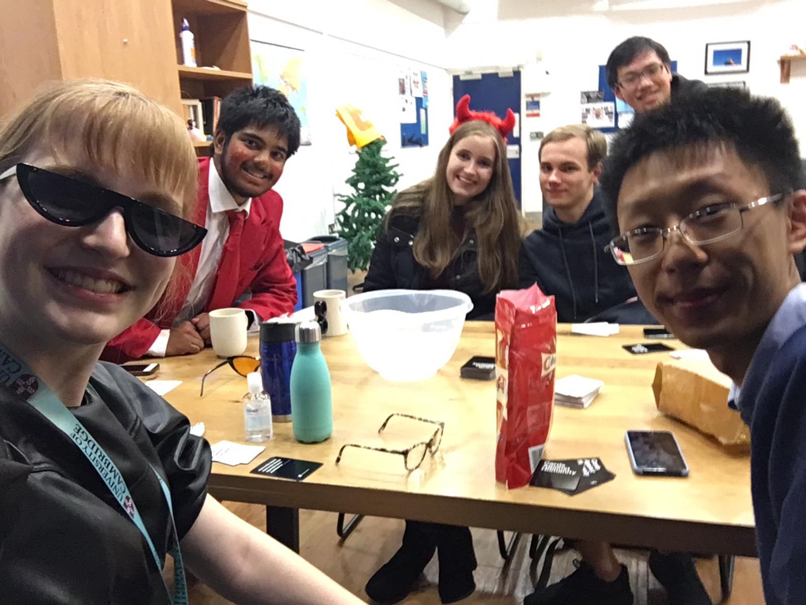 Six students in various levels of fancy dress, sat around a table