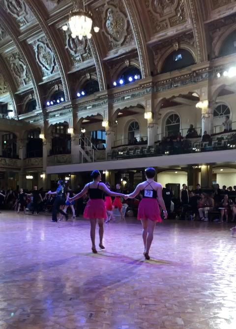 Two students dancing in a ballroom with decorated ceilings