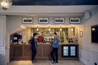 Two students leaning against the bar of the Buttery in Christ's College, Cambridge.