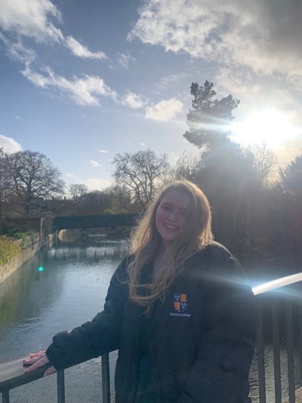 Emily stood in front of river Cam in a Christ's puffer jacket