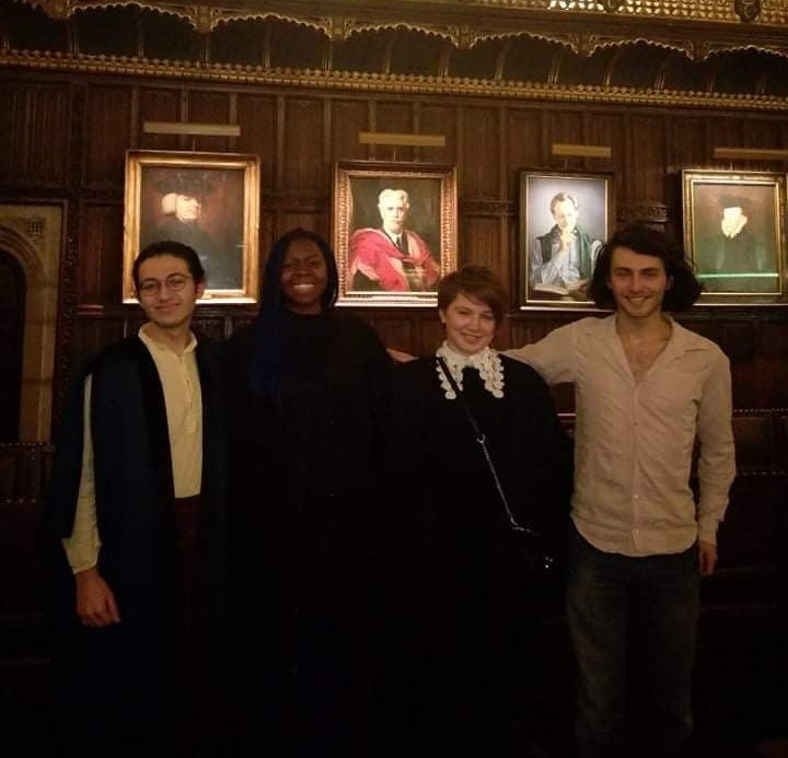 Four students stood in front of some portraits, in Formal Hall