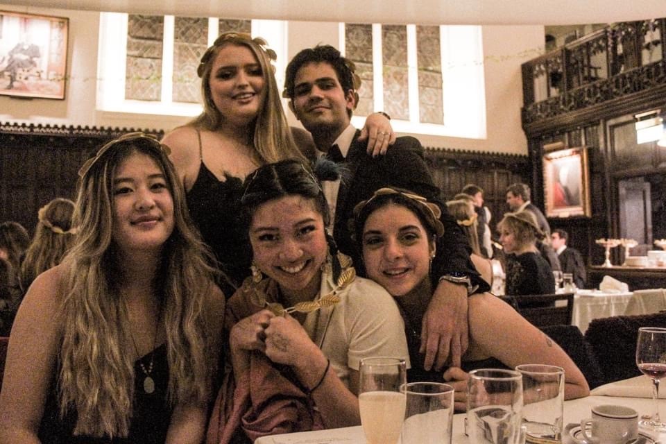 five students, dressed up in front of a table in Formal Hall