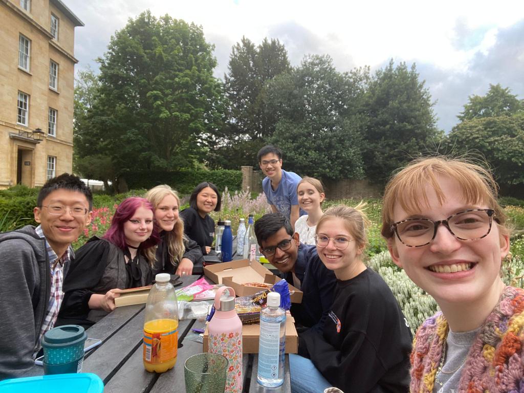 Nine students sat at a picnic bench, eating pizza