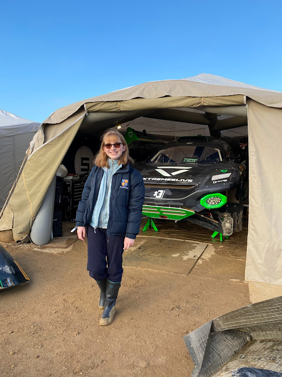 Sophie in front of a motorsports car, wearing a Christ's college coat