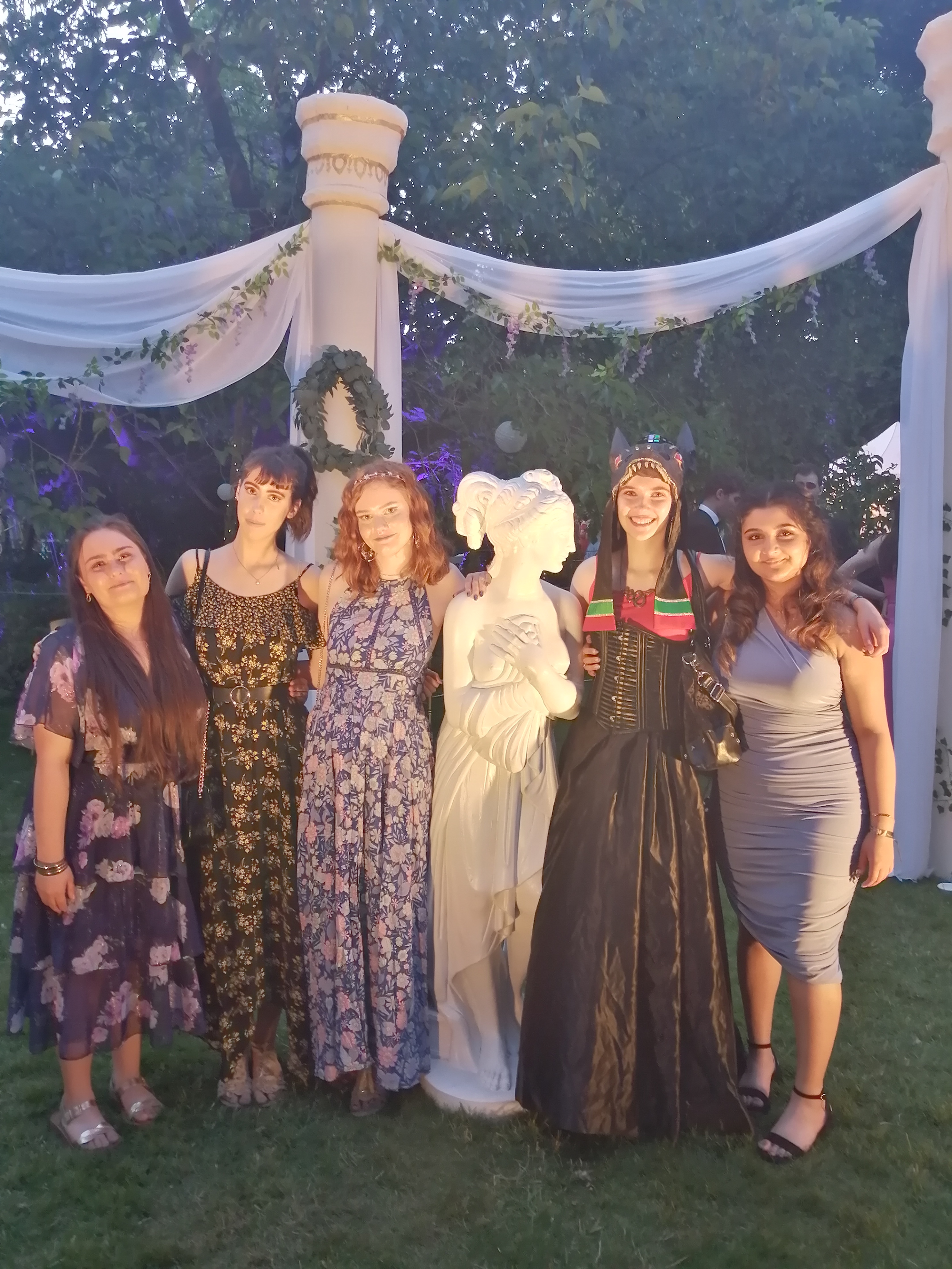 Five students in formal outfits, stood with a greek-style statue