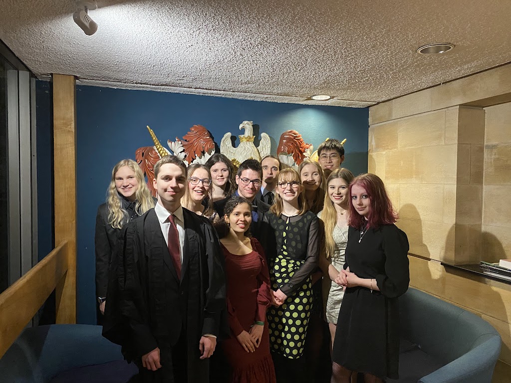 A group of 12 people in formal dress, stood in the space under Christ's library