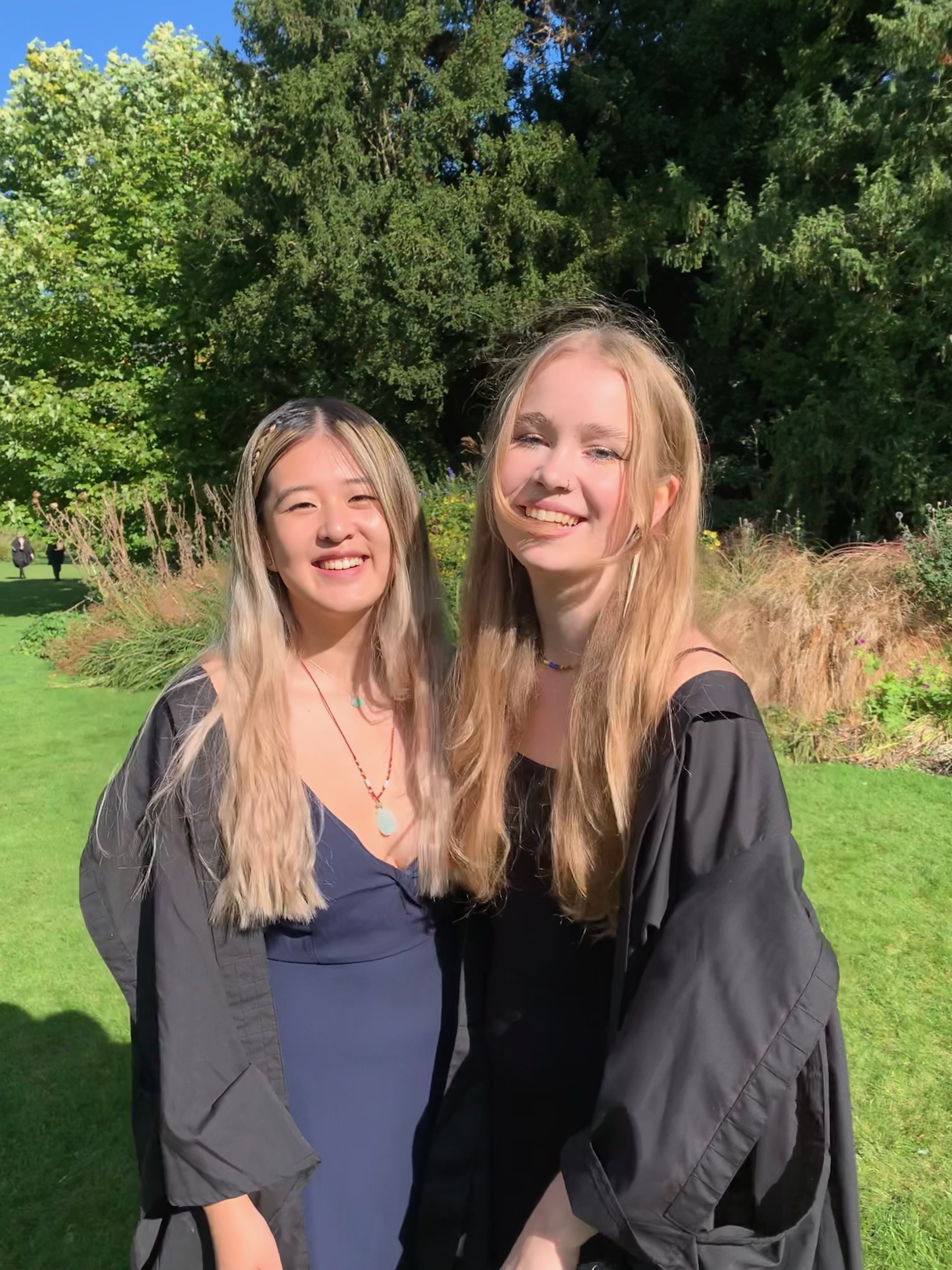 Two students in gowns in the Fellows' garden, smiling