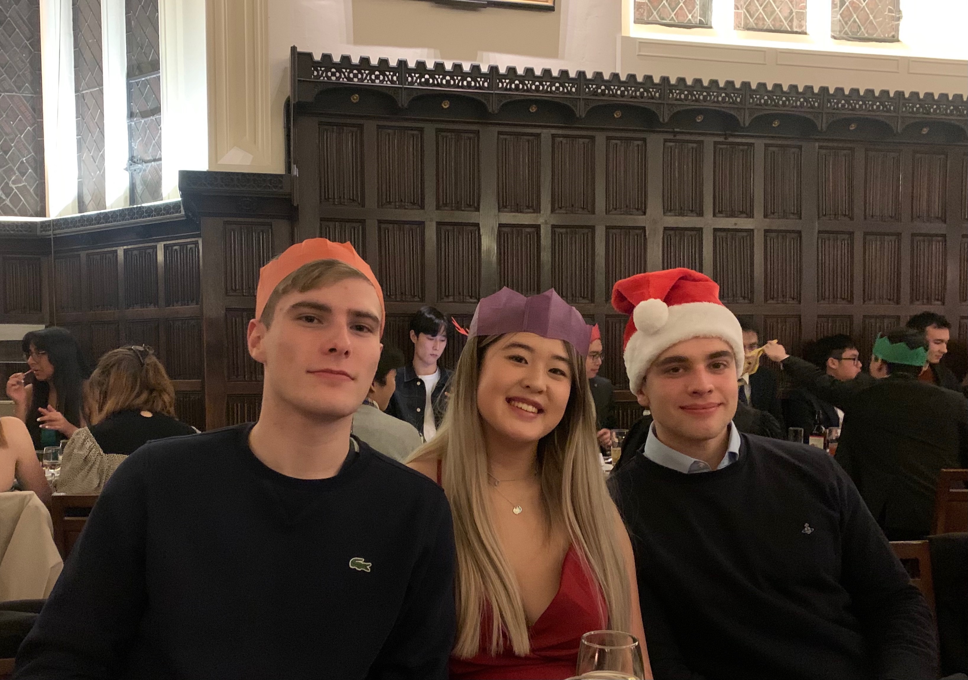 Three students with paper crowns/santa hats in formal hall