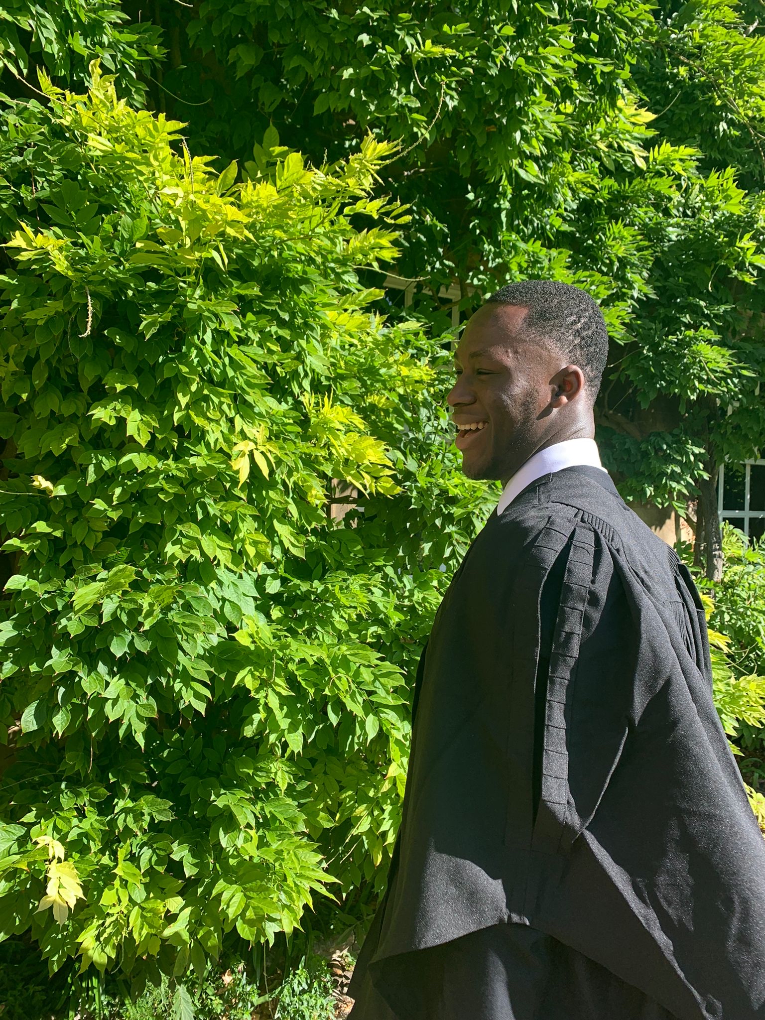 Ayomide in his matriculation gown, in front of greenery