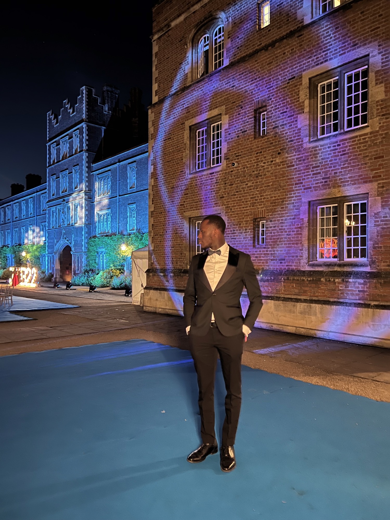 Ayo standing in front of a buiding with coloured lights projecting onto it, in formal dress