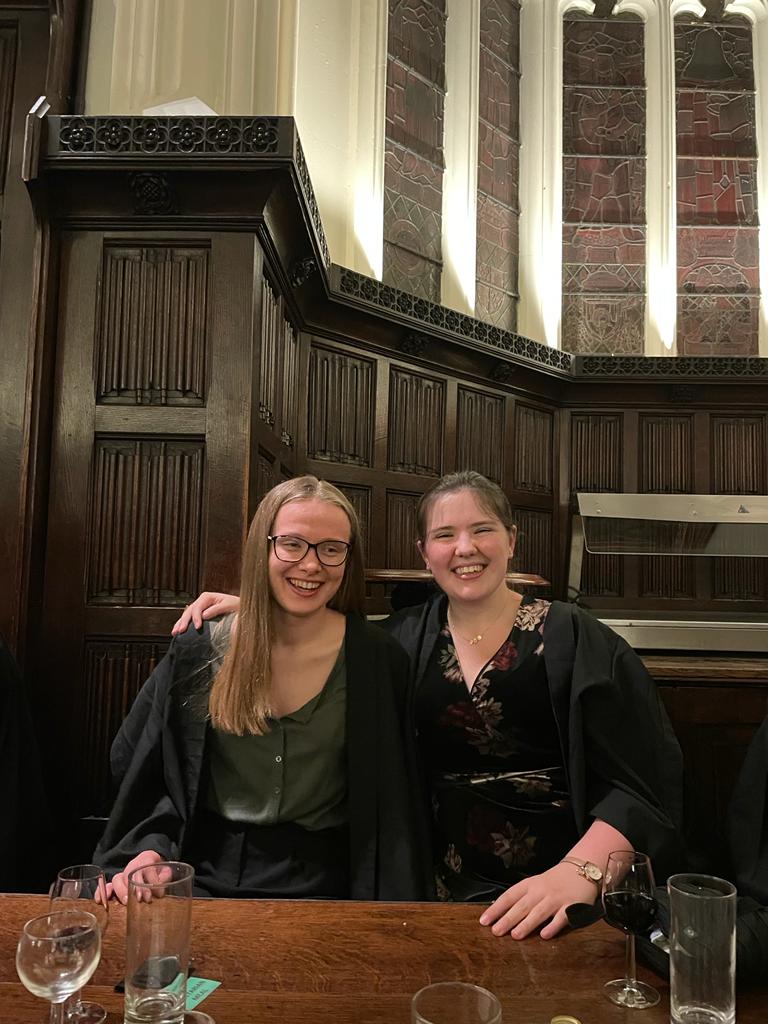 Two women wearing formal dress and laughing, sat in Christ's formal hall
