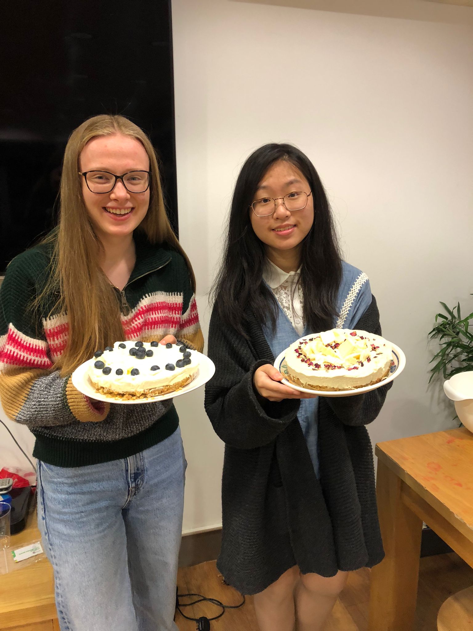 two women holding cheesecakes, decorated with fruit