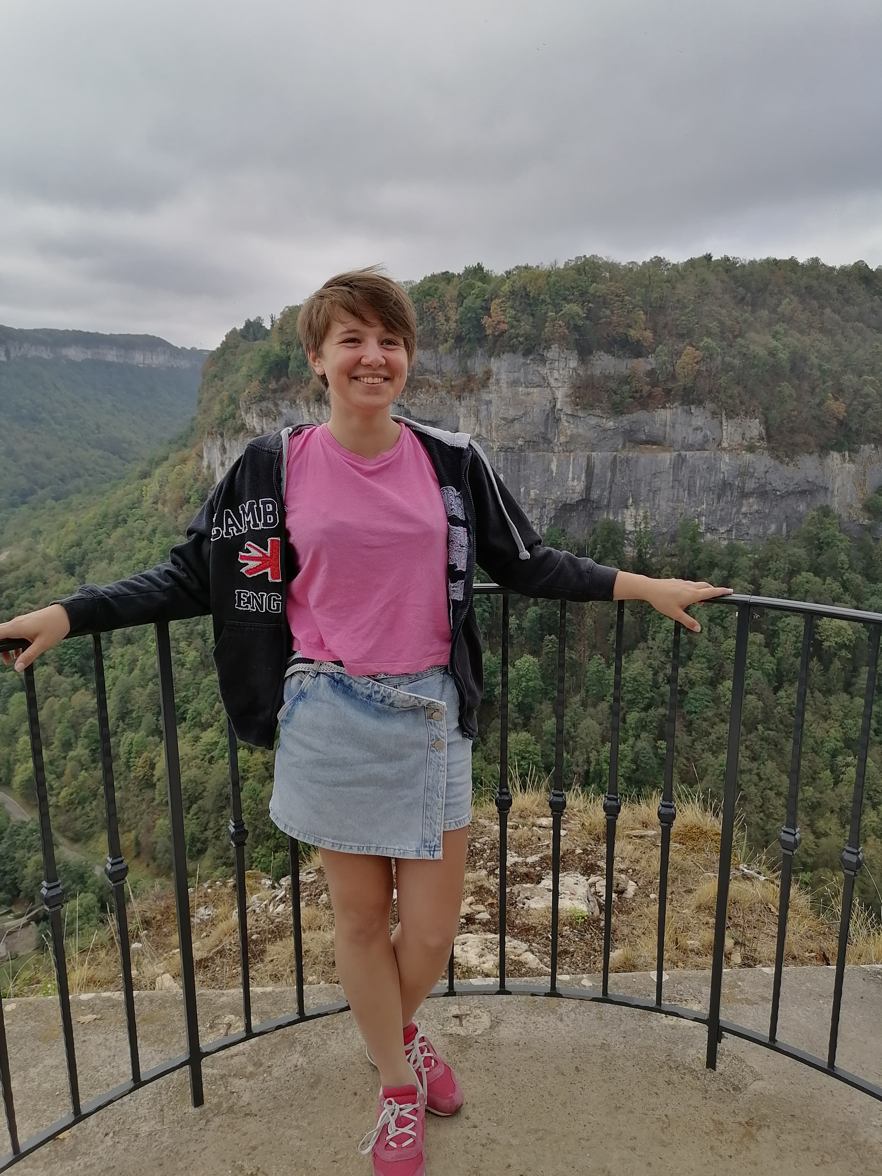 A student stands in front of some mountains, with her hands on some railings behind her