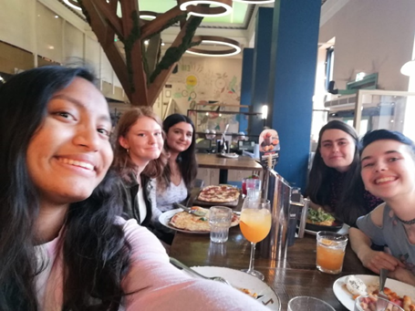 A selfie of five students sat around a table