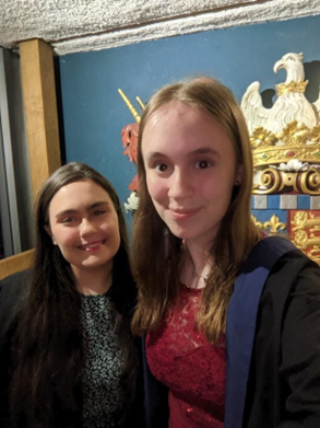 Selfie with two students in front of a gold christ's logo, in the space under the library