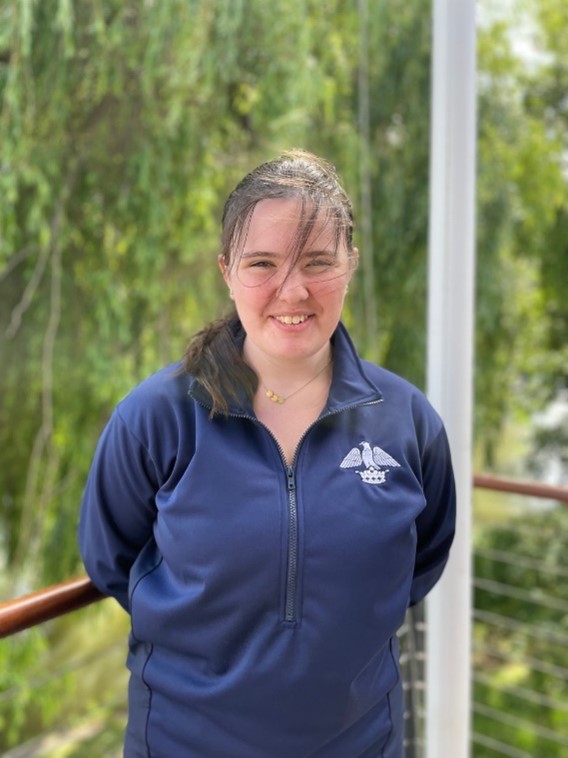 A student in a rowing jacket, stood in front of some greenery