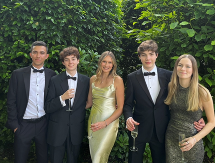 Five students in formal outfits in front of greenery