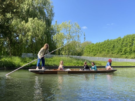 A punt (long boat driven by someone with a pole) with five students in it
