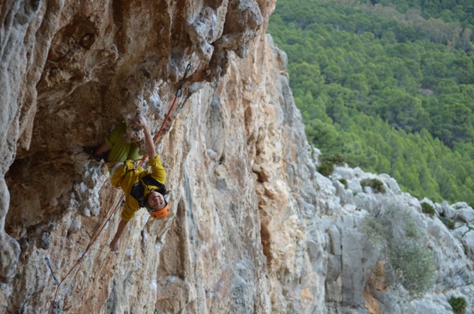 Ari hanging off a cliff face, in climbing gear