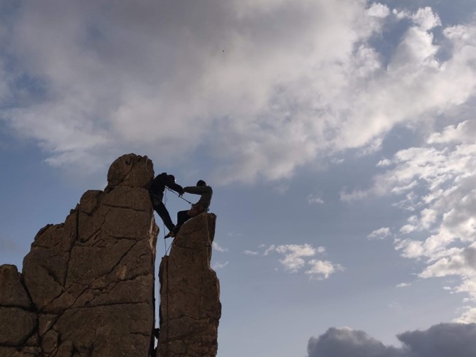 Two people on a rock, in climbing gear, making a heart shape with their bodies