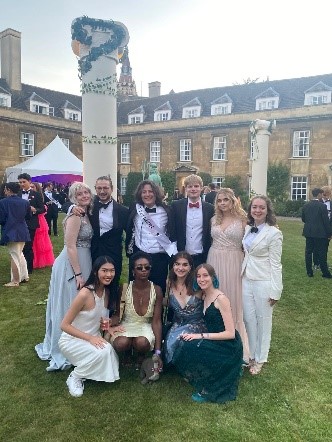 Ten students, dressed up on first court lawn, with a greek-style pillar in the background