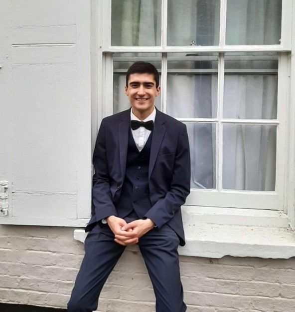 A student in black tie, sat on a windowsill