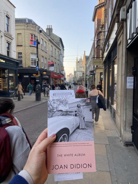 A hand holding a book, in front of a busy Cambridge street