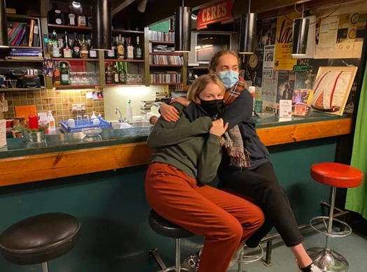 Two students hugging, sat at a bar