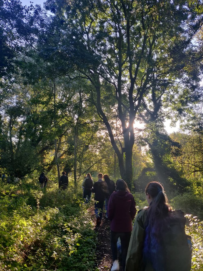 walking through some woodland, with the backs of a few people in front visibile. 