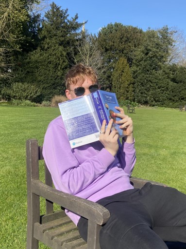 A student sits with their eyes peeking over a book