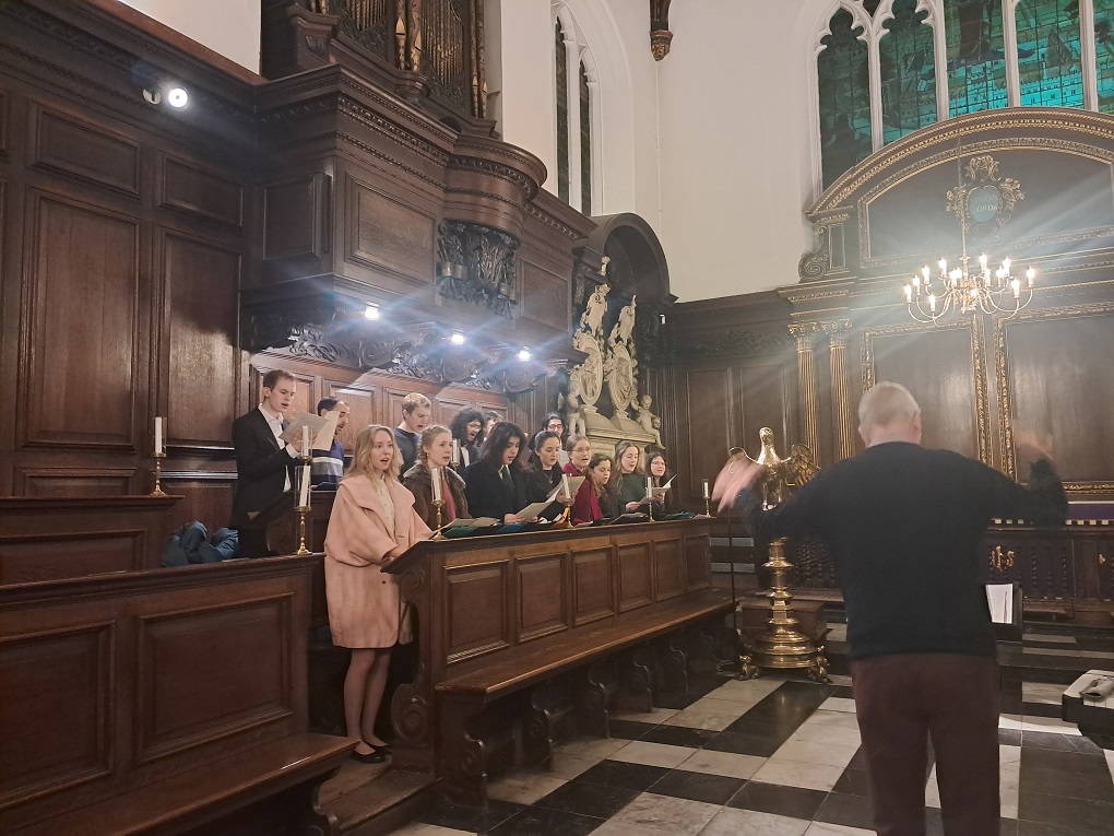 A group of people singing in a chapel with conductor