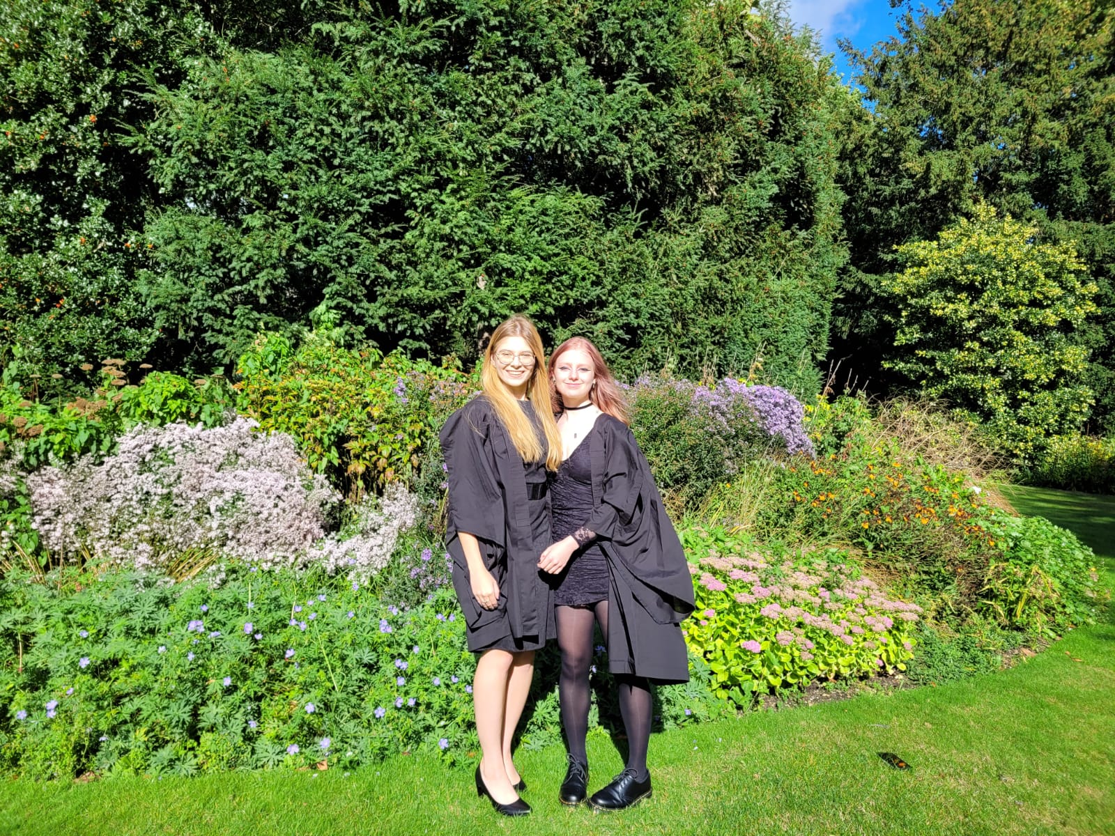Two students in gowns, in front of some greenery
