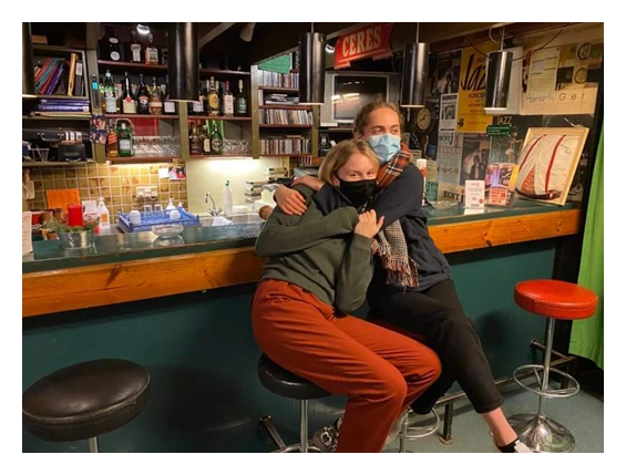 Two students hugging, sat at a bar