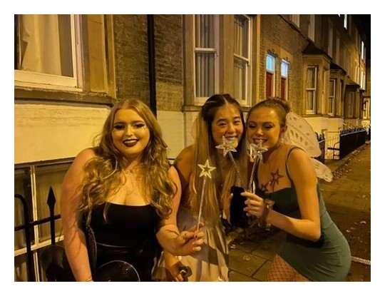 Three women stood in front of a row of terraces (Jesus lane), dressed in halloween outfits