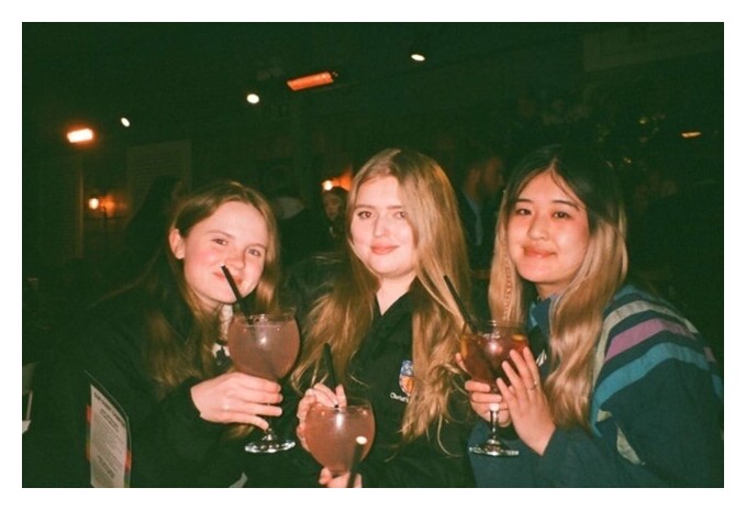 Three women holding drinks, smiling at the camera