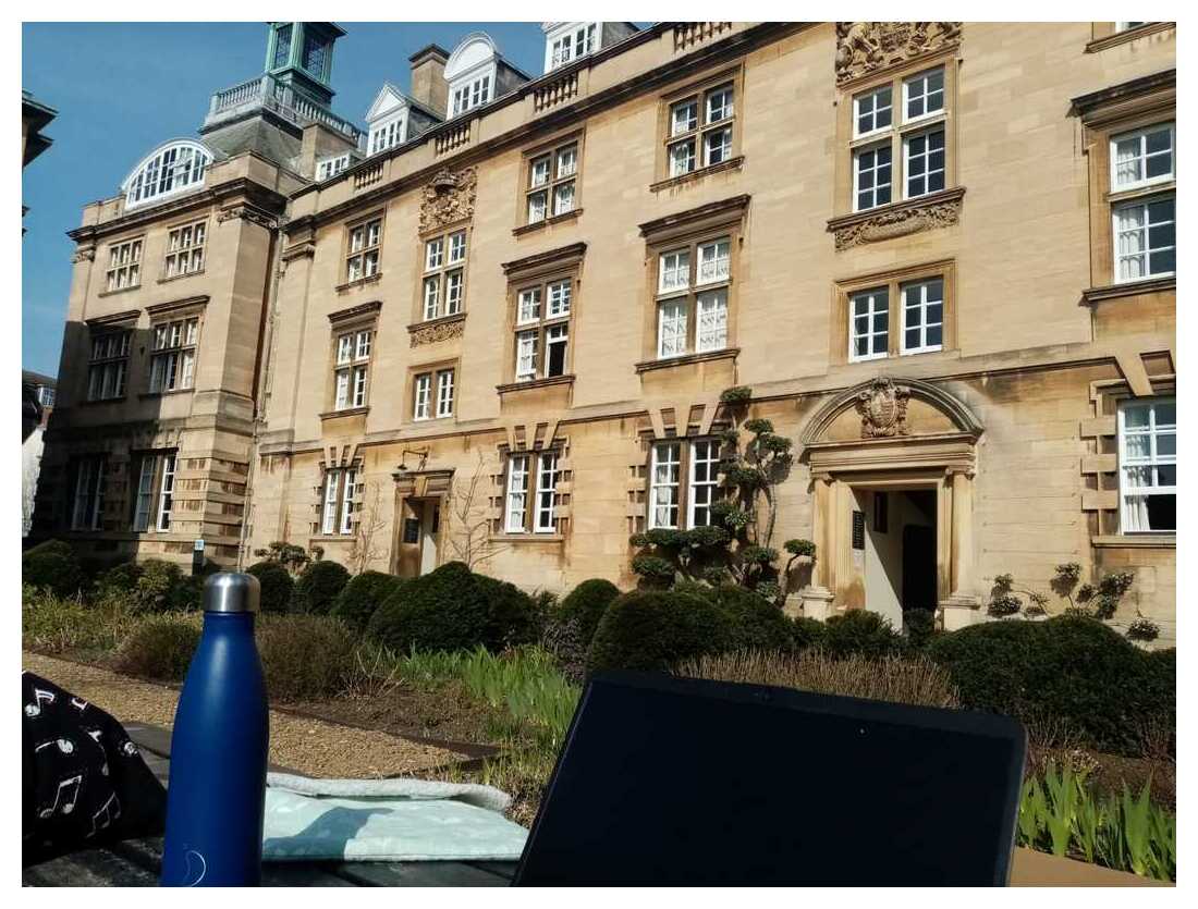 A laptop and water bottle, with a Christ's building behind