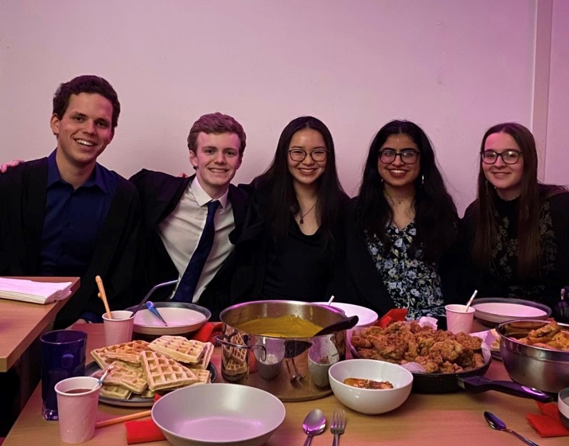 A group of five in front of a big table of food, smiling