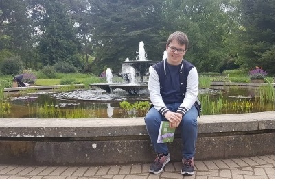 Adam sat on the edge of a fountain in a park, smiling.