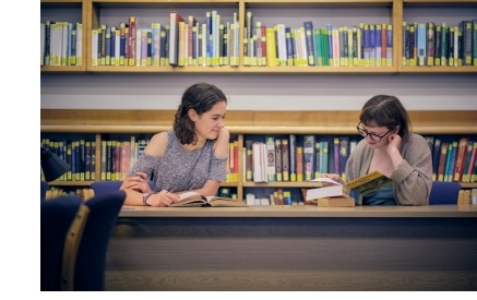 Two female students, sitting at a desk and reading books, in the library of Christ's College, Cambridge.