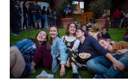 A group of students sat, leaning on eachother, on a well-kept lawn