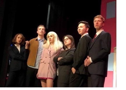 A candid shot of a group of actors, in formal dress, onstage in mid-performance.